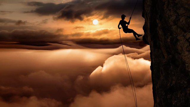 Cinemagraph Continuous Loop Animation. Silhouette of a Unrecognizable man rappelling down a steep cliff on top of a mountain during a sunny and cloudy vibrant sunset or sunrise.