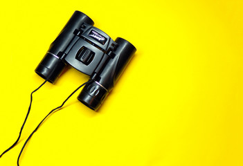 Binoculars. Binoculars on a yellow background with a copy space view from above. Concept of observation and tourism. Background with binoculars. The binoculars are isolated. Template for the design.