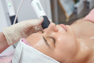 Doctor cosmetologist makes apparatus massage on the skin of the face of a young woman, close-up