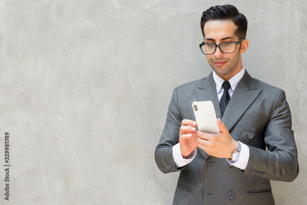 Wall mural Young handsome Persian businessman using phone against concrete wall outdoors