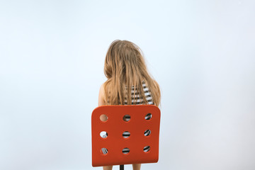 Girl sitting on red chair. Mental health concept. Teenager in depression. Kid at reception of psychologist. Sadness and bad mood. Background with copyspace. Stock photo.