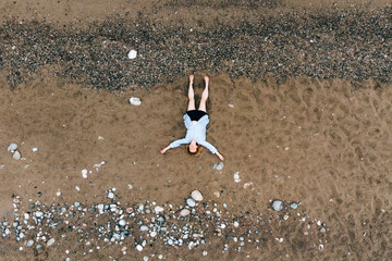 Aerial view of young woman lying on beach. Pretty girl on sand, view from drone. Attractive lady enjoying summer vacation, recreation concept. Beauty on seashore. Seashells on sand from above