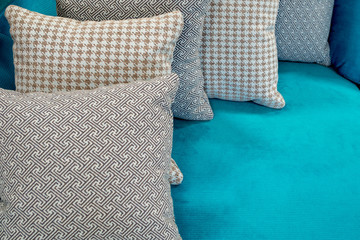 Middle size puffy pillows with patterned upholstery in gray, beige and brown colors lying one after the other on the light blue fabric upholstery of the sofa. Abstract interior design background.