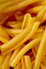 Randomly scattered appetizing raw dry yellow noodles, extreme macro, vertical. Abstract food pattern for poster or background.
