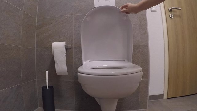 white faience toilet in the toilet room, girl closes the lid with her hand, the concept of germs, cleanliness, health