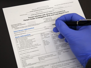 Fototapeta na wymiar Gloved Hand Filling Out a Coronavirus Report Form