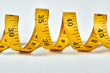 Yellow color centimeter with black figures for measurement of length and width on a white background. Measuring tape of the tailor for you design. Closeup, selective focus