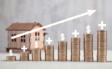  Wooden house model with coins on white table with profit graph.