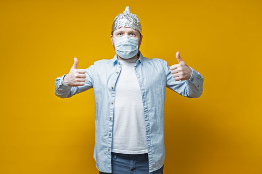 Man protected himself from the virus, put on a medical mask and a tin foil hat, he makes a thumbs up gesture and looks joyfully.