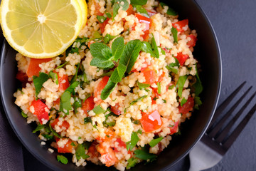 Tabbouleh salad in black bowl with a fork on black stone surface close-up. Flat lay composition