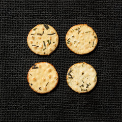 Four baked rice crackers with flecks of seaweed on a black cloth background