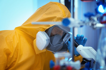 Scientist in chemical protective suit using microscope at laboratory. Virus research