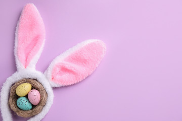 Headband with Easter bunny ears and dyed eggs in nest on violet background, flat lay. Space for text