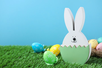 Fototapeta na wymiar Easter bunny figure and dyed eggs on green grass against light blue background. Space for text
