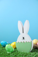 Easter bunny figure and dyed eggs on green grass against light blue background