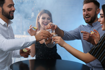 Young people toasting with Mexican Tequila shots at table in bar - Powered by Adobe