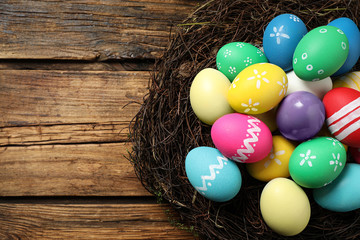 Colorful Easter eggs in decorative nest on wooden background, top view