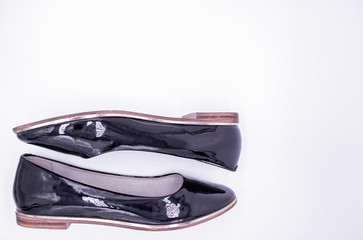 A pair of black patent leather shoes with a low heel and a gold stripe along the sole on a white background