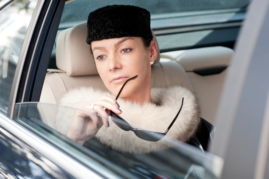 Luxury woman with fur and sunglasses in the back seat of a car