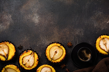 Pears and custard mini tarts on a dark brown concrete old table background. Top view.