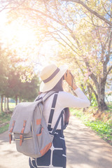 Smiling woman traveler in pink sakura blossom park at doi inthanon landmark chiang mai thailand with backpack holding vintage camera on holiday, relaxation concept, travel concept