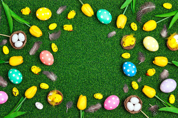 Easter frame with colored eggs, chickens and tulips on a green grass background.