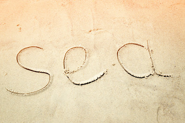The word sea on the beach sand at sunset
