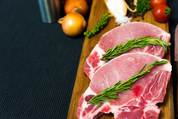 Raw pork chop meat on wood plate with vegetables, spices, salt and black pepper in dark black cloth table
