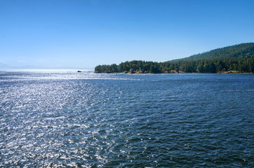 beautiful Southern Gulf Islands in the Strait of Georgia from the ferry. Islands with evergreen conifers and turquoise sea water on a bright sunny day. Trip from Vancouver to Victoria, Canada