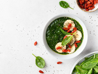 Spinach and banana smoothie bowl with chia seeds, goji berries and banana slices. Green healthy protein and vitamins breakfast or snack. Vegetarian and detox diet concept. Top view, copy space.