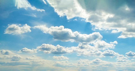 Blue sky with soft white clouds. Cumulus clouds with breaking sunlight. Rays from the sun.