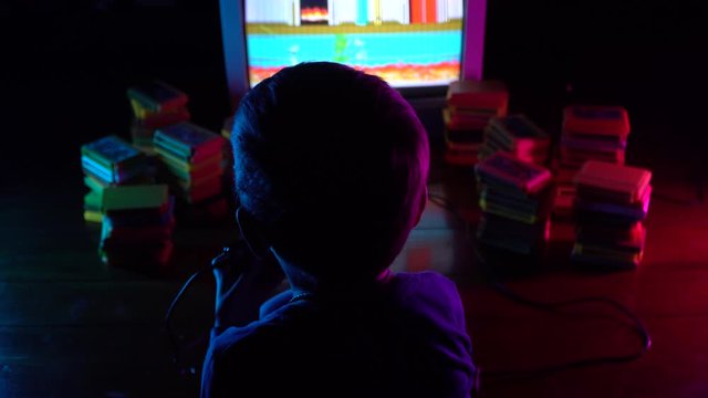 Little boy playing in retro console. Neon lighting.A view from the shoulders