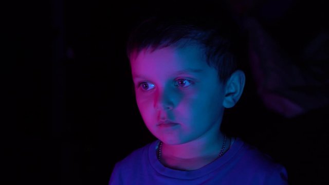 A little boy sits in front of the TV playing in a retro console. Neon lighting.Close up