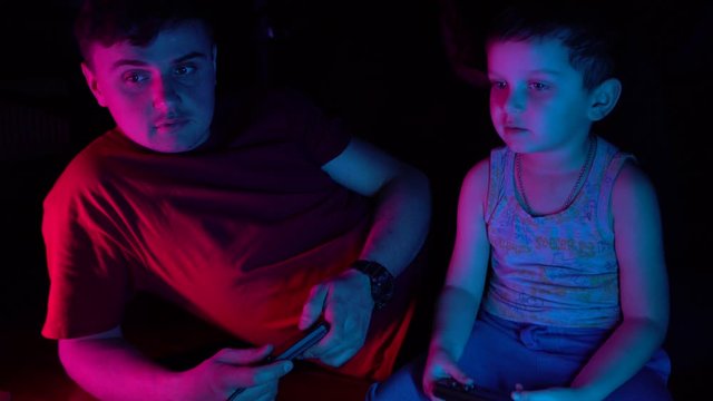 Little boy with his father talking and playing in retro consol. Son having fun with his father.Neon lighting