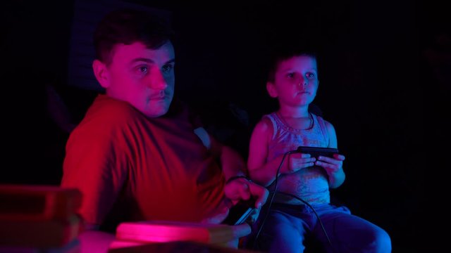 Little boy with his father playing in retro consol. Son having fun with his father.Neon lighting
