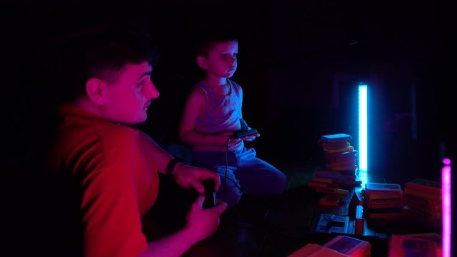 Little boy with his father playing in retro consol. Son having fun with his father.Side wiev.Neon lighting