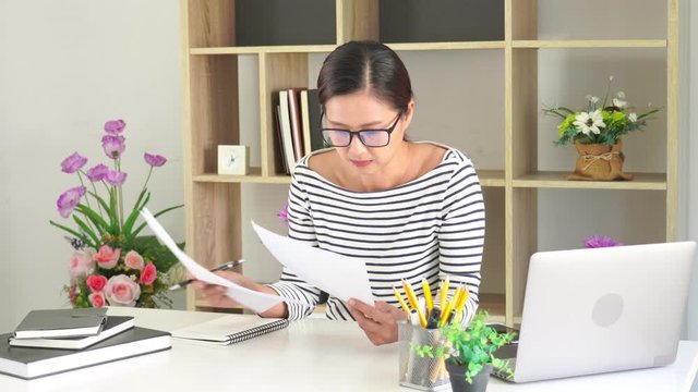 4k video of asian learning girl with reading a book or report data sheet with papers for study sitting by wooden table, Education and lifestyle concept.