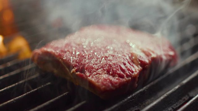 Delicious juicy meat steaks cooking on the grill on fire. Aged prime rare roast grilling tenderloin fresh juicy beef filet with lines slow motion. Grill, tasty beefsteak