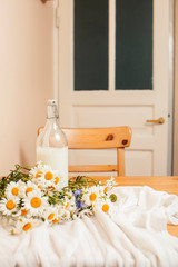 Simply stylish wooden kitchen with bottle of milk and glass on table, summer flowers camomile, healthy foog moring concept