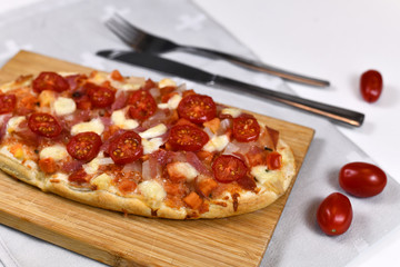 Homemade oval shaped pizzas topped with mozzarella cheese, tomato and salami sausage on wooden board