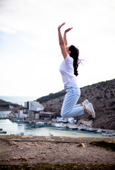 Fashion style woman jump on the top and look at city.  The traveler looking to the cityscape panorama by the sea. Girl succesfully travels