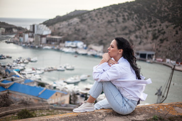 Fototapeta na wymiar Fashion style woman sit on the top and look at city. The traveler looking to the cityscape panorama by the sea. Girl succesfully travels