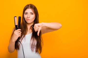 A young woman straightens her hair with a hair straightener. Damage to hair caused by a hot hair...