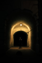 the silhouette of a man in a dark arch illuminated by a lamp