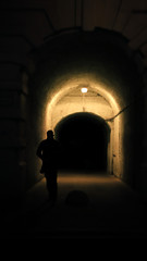 the silhouette of a man in a dark arch illuminated by a lamp