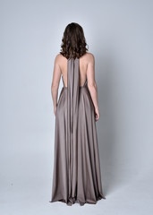  Portrait of a pretty brunette girl wearing a long silver evening gown, full length standing pose...