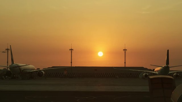 Silhouettes of large passenger airplanes in airports during sunset, planes taking off and landing on background - transportation concept 4k footage
