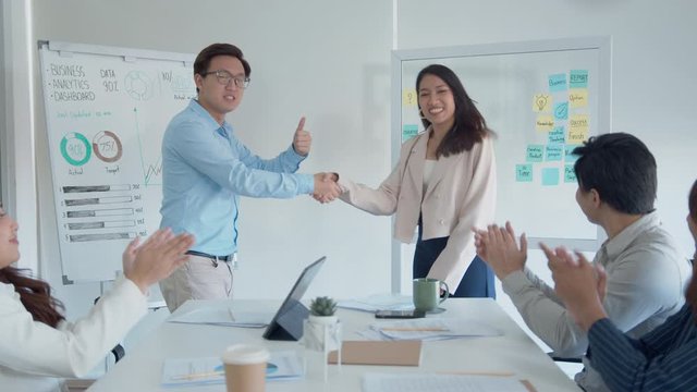 Asian Male Manager Handshaking Young Businesswoman after presentation project, get a promotion celebrating a successful project while colleagues clapping hand applause appreciation in the office board