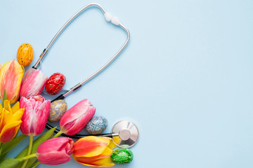Stethoscope with colorful eggs and tulips on a blue background. copy space