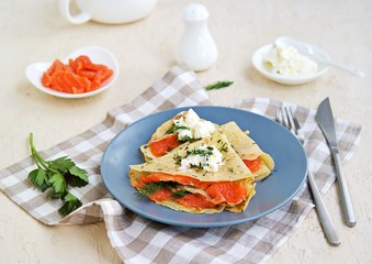 Thin crepe pancakes with salted salmon and cream cheese on a gray plate on a light concrete background. French cuisine. Pancake Day.